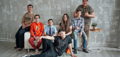 Group of seven people posing casually in a stylish indoor setting with a concrete wall background.
