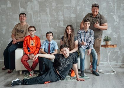Group of seven people posing casually in a stylish indoor setting with a concrete wall background.